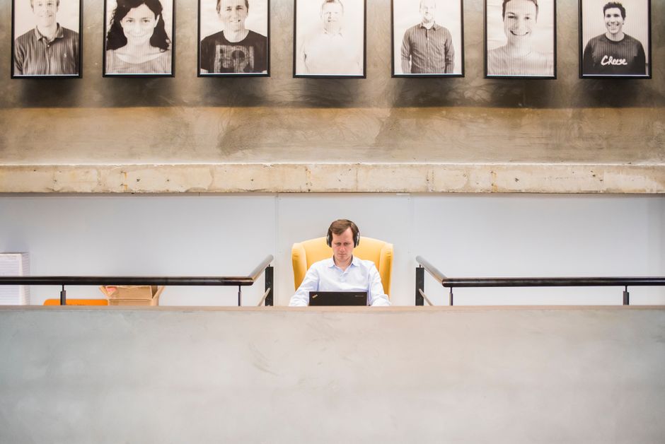 Business professional working on a laptop in a contemporary office setting with framed portraits above.