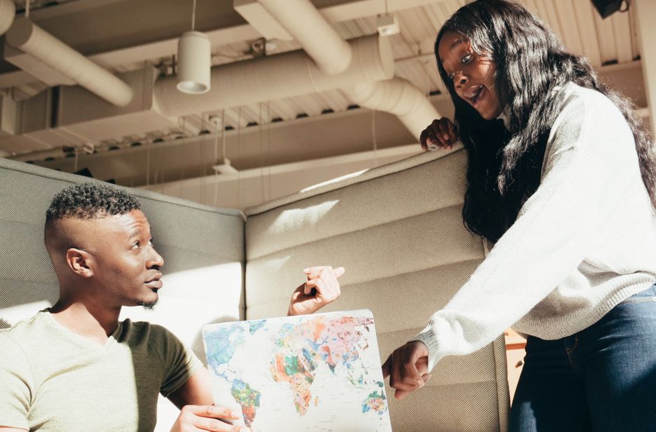 Two colleagues engaging in a discussion with a world map in a modern office setting.