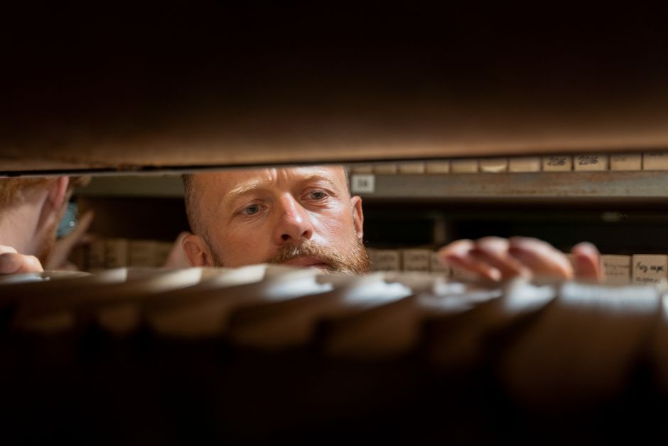 A man searches through archives in an office storage room, focused and working.